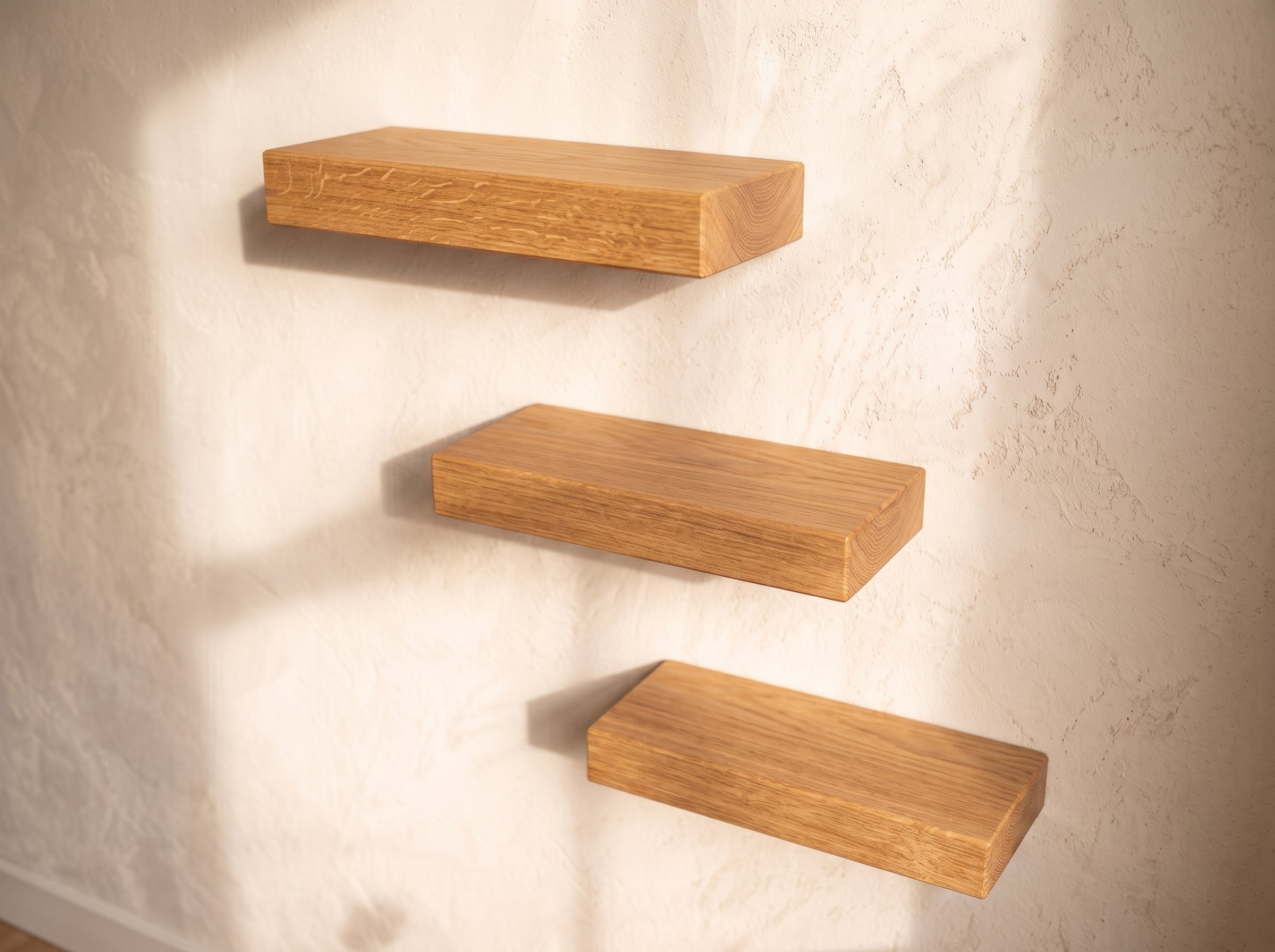 Three floating wooden shelves in a warm medium-brown finish, mounted on a textured off-white plaster wall with soft natural shadows.