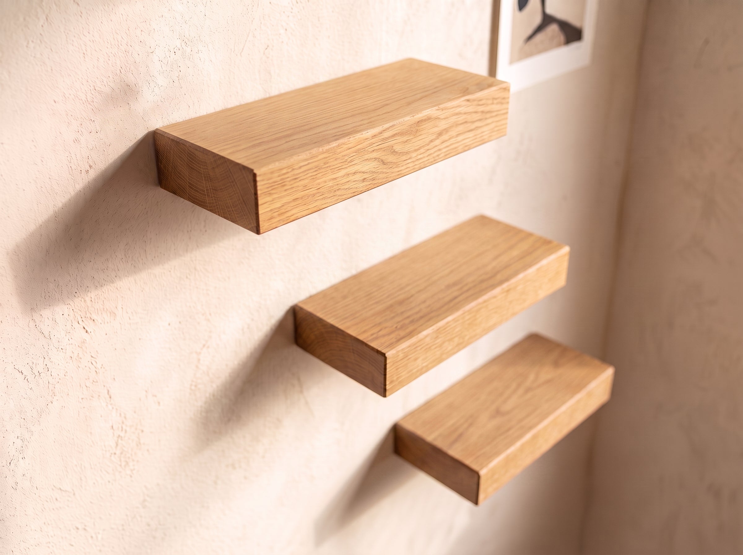 Three floating wooden shelves in a light oak finish mounted on a textured beige plaster wall.