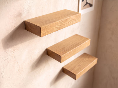 Three floating wooden shelves in a light oak finish mounted on a textured beige plaster wall.