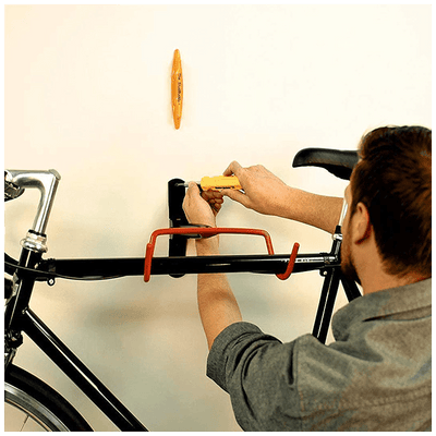 The StudBuddy® Stud Finder by The Mortise & The Hare detects wall studs, showing a display with LED indicators on a wall surface.